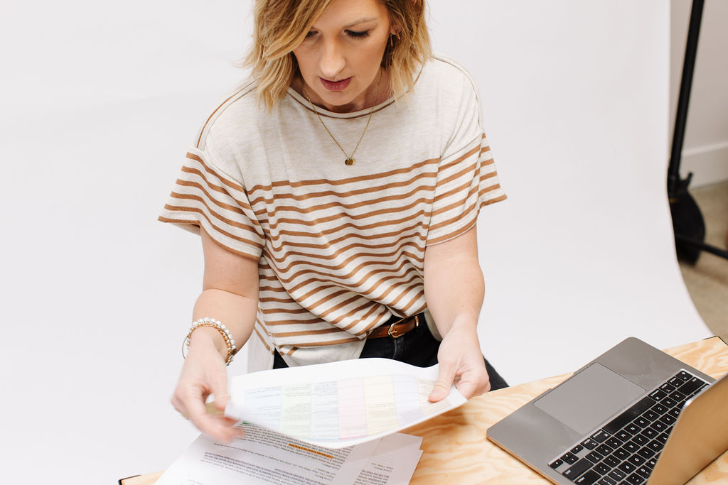 Female entrepreneur analyzing website organization and About page content on her computer with research materials nearby